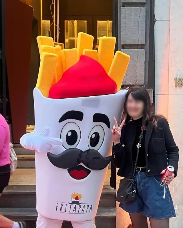 Papa, la mascotte Fritapapa, pose sur un tapis rouge devant l’entrée de la friterie avec une visiteuse.